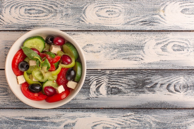 Vista superior Ensalada de verduras frescas con pepinos en rodajas, tomates, aceitunas y queso blanco dentro de la placa en el color de comida de ensalada de verduras de escritorio gris