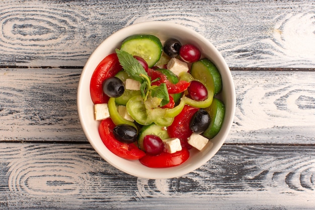 Vista superior ensalada de verduras frescas con pepinos en rodajas, tomates, aceitunas y queso blanco dentro de la placa en el escritorio gris ensalada de comida vegetal color de comida