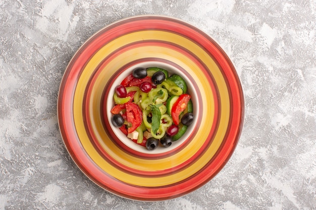 Vista superior Ensalada de verduras frescas con pepinos en rodajas, tomates, aceitunas y queso blanco dentro del plato en la mesa gris, comida vegetal, ensalada, comida, merienda.