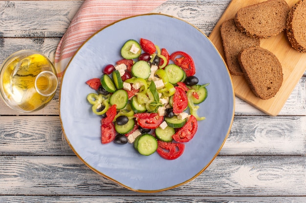 Vista superior Ensalada de verduras frescas con pepinos en rodajas, tomates, oliva, placa interior con aceite y pan en la superficie gris, comida vegetal, ensalada, color de comida