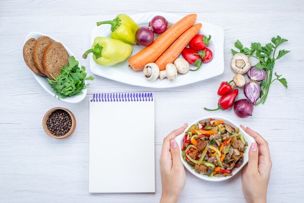 Vista superior de ensalada de verduras frescas en rodajas con carne junto con hogazas de pan y verduras y verduras enteras a la luz, plato de vitamina de ensalada de comida