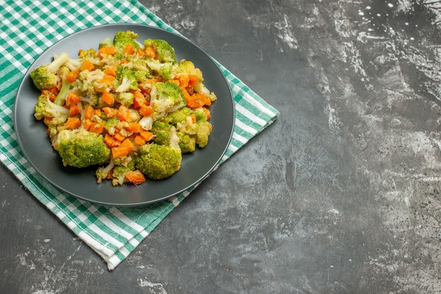 Vista superior de ensalada de verduras frescas y saludables en una toalla despojada verde en la mesa gris