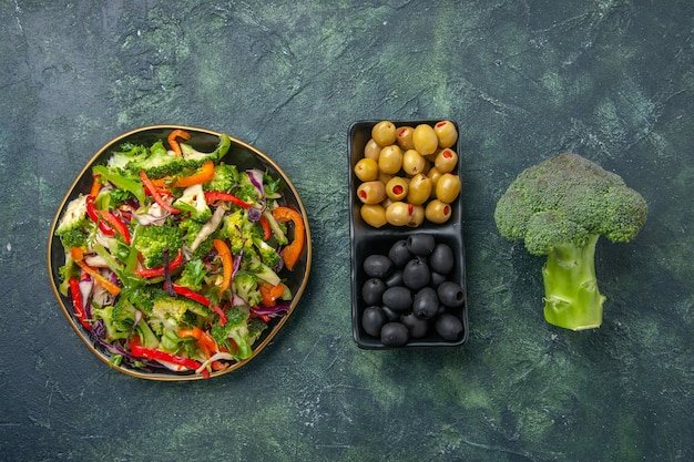 Vista superior de ensalada de verduras en un plato brócoli de aceitunas verdes y negras sobre fondo oscuro