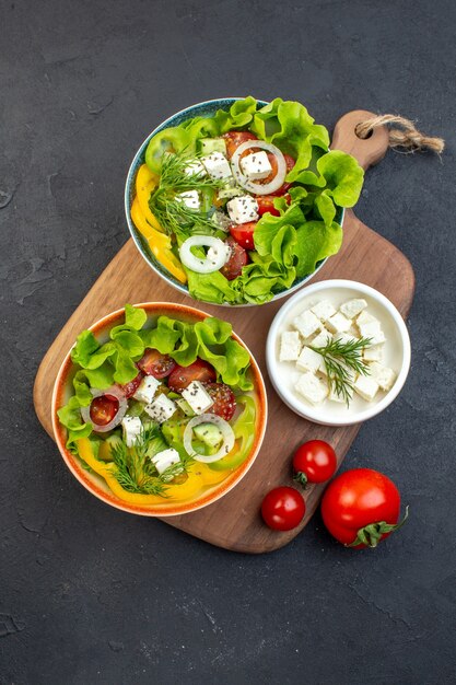 Vista superior de ensalada de verduras con queso, pepinos y tomates sobre fondo oscuro