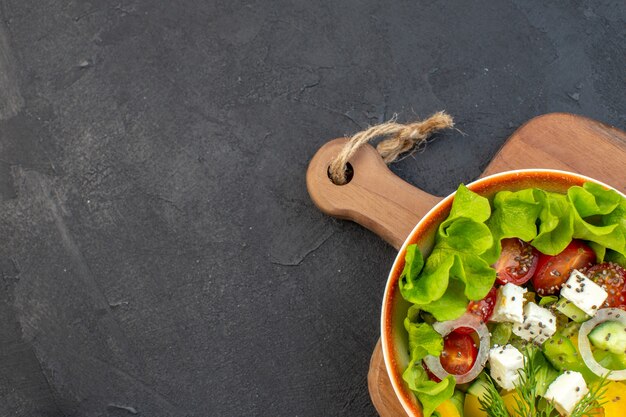 Vista superior de ensalada de verduras con queso y tomates sobre fondo oscuro