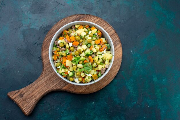 Vista superior ensalada de verduras en rodajas salpicado con rodajas de pollo dentro de la placa en el escritorio azul oscuro