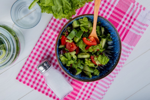 Vista superior de ensalada de verduras y sal sobre tela escocesa con agua desintoxicante y lechuga sobre superficie de madera