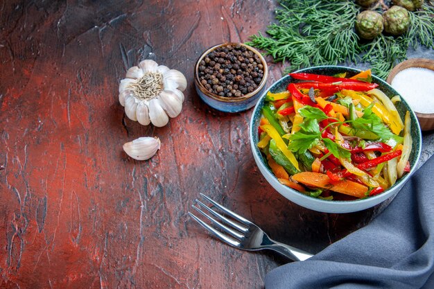Vista superior de ensalada de verduras en un tazón azul ultramarino mantón ajo pimienta negra tenedor sobre mesa rojo oscuro
