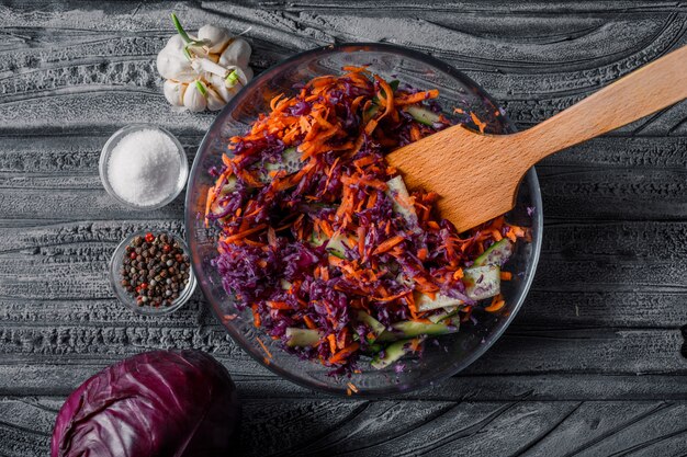 Vista superior ensalada de verduras en un tazón con especias en la mesa de madera oscura