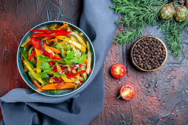 Foto gratuita vista superior de ensalada de verduras en un tazón de pimienta negra rama de abeto chal azul ultramar en mesa rojo oscuro