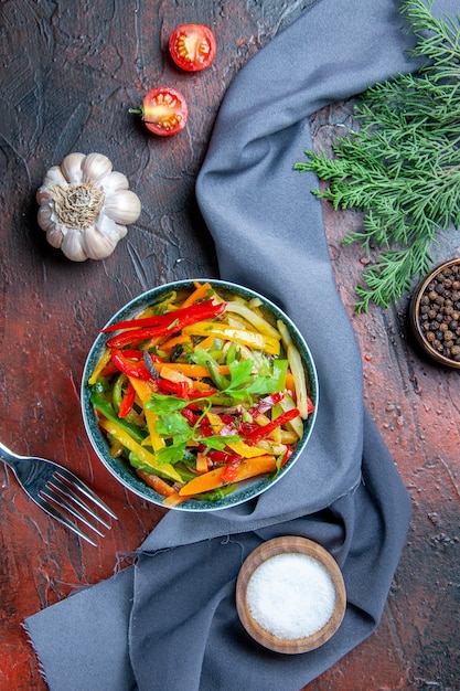 Vista superior de ensalada de verduras en un tazón de pimienta negra rama de abeto mantón azul ultramarino sal de ajo en la mesa de color rojo oscuro