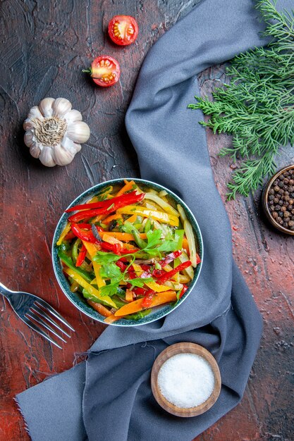 Vista superior de ensalada de verduras en un tazón de pimienta negra rama de abeto mantón azul ultramarino sal de ajo en la mesa de color rojo oscuro