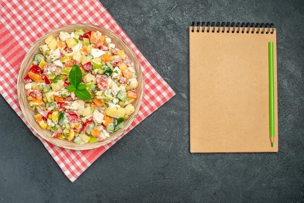 Vista superior de la ensalada de verduras en un tazón sobre una servilleta roja con el bloc de notas en el lateral sobre fondo gris oscuro