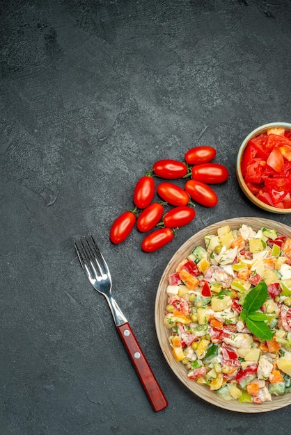 Vista superior de ensalada de verduras con tomates y tenedor sobre fondo gris oscuro