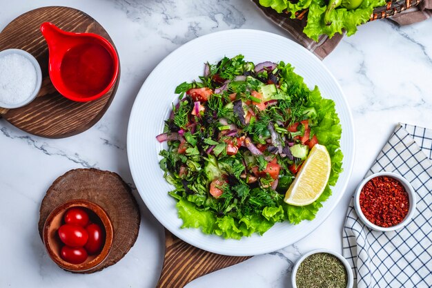 Vista superior ensalada de verduras con verduras sobre lechuga en un plato con una rodaja de limón y tomates cherry