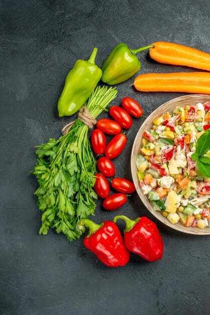 Vista superior de ensalada de verduras con verduras a su alrededor sobre fondo gris oscuro