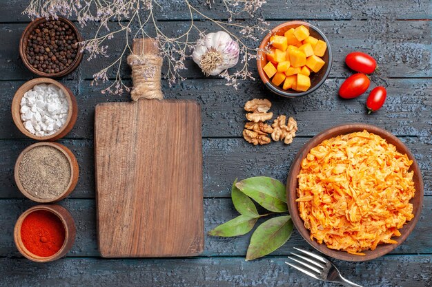 Vista superior ensalada de zanahoria rallada con ajo, nueces y condimentos en el escritorio oscuro ensalada de dieta saludable color naranja maduro