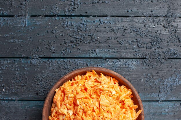 Vista superior de la ensalada de zanahoria rallada dentro de la placa en el color azul oscuro de la ensalada de escritorio rústico verduras de dieta de salud madura