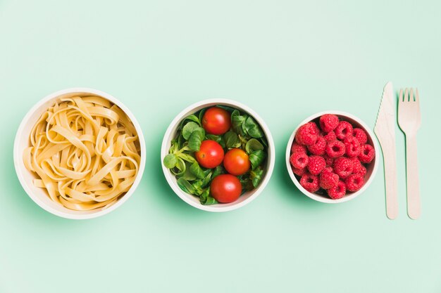 Vista superior de envases de alimentos con frambuesas, ensalada y pasta.