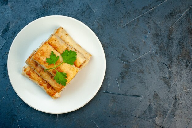 Vista superior de envolturas de lavash fritas en un plato servido con verde en el lado derecho sobre fondo oscuro