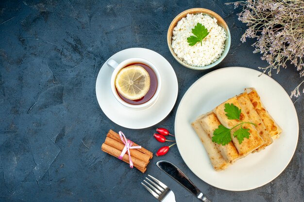 Vista superior de envolturas de lavash en un plato servido con queso verde y cubiertos rallado en un tazón limones canela una taza de té negro con limón sobre fondo negro