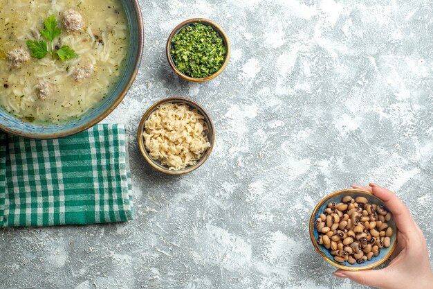 Vista superior erishte en tazón diferentes materias en tazones de frijol bol en mano de mujer sobre fondo gris