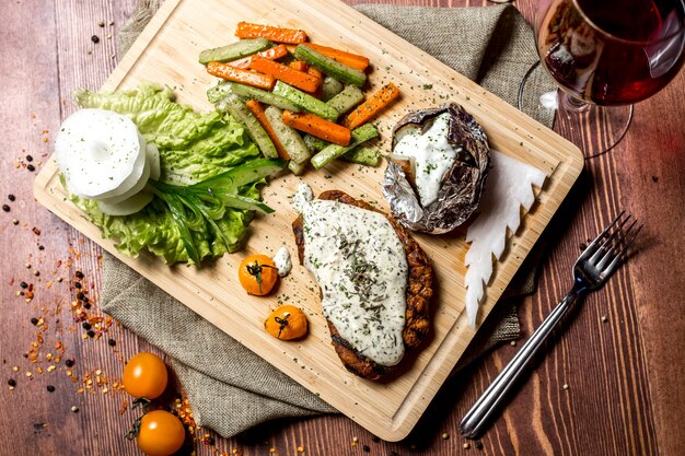 Vista superior de escalope con queso crema con papas al horno en papel de aluminio y con verduras en un tablero