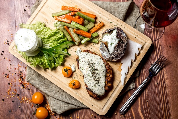 Vista superior de escalope con queso crema con papas al horno en papel de aluminio y con verduras en un tablero