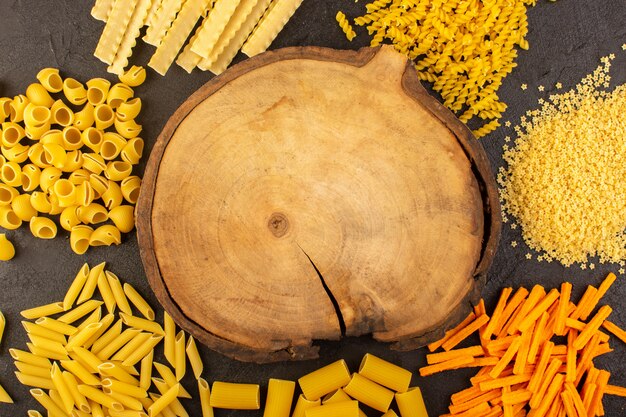 Una vista superior escritorio de madera marrón junto con diferentes pastas crudas amarillas formadas aisladas en la oscuridad