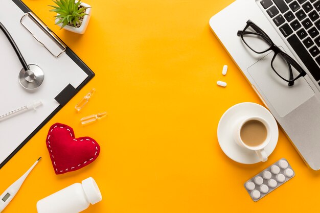 Vista superior del escritorio del médico con taza de café; portátil contra el fondo amarillo