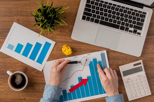 Vista superior del escritorio de oficina con computadora portátil y tabla de crecimiento analizada por las manos