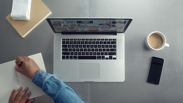 Vista superior del escritorio de trabajo arriba con una computadora portátil y una taza de café y notas de papel de la mano del hombre Vista superior del hombre trabajando desde arriba