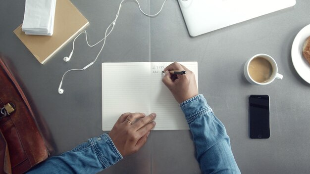 Vista superior del escritorio de trabajo arriba con una computadora portátil y una taza de café y notas de papel de la mano del hombre Vista superior del hombre trabajando desde arriba