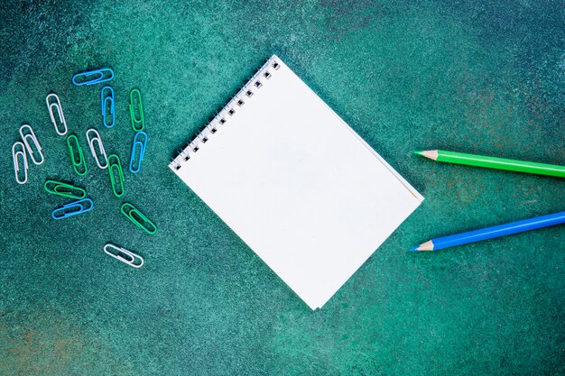 Vista superior espacio de copia lápices de color verde claro y azul con clips y bloc de notas sobre un fondo verde