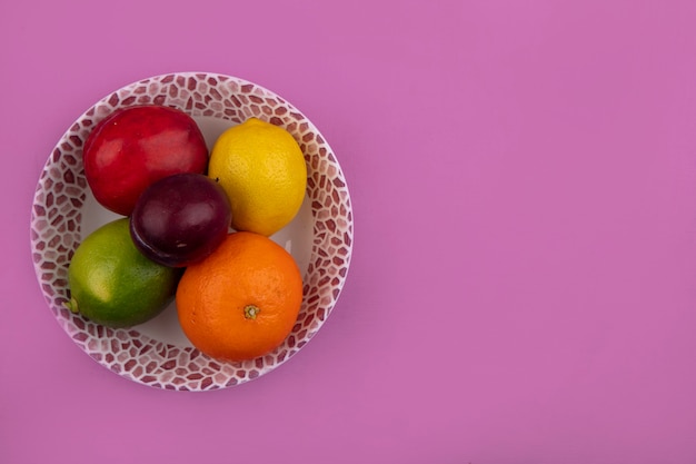 Vista superior espacio de copia limón con limón, melocotón, ciruela y naranja en un plato sobre un fondo rosa.