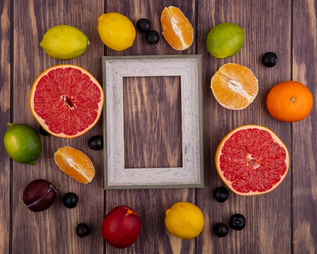 Foto gratuita vista superior del espacio de copia marco de bola gris con melocotón limones limas naranja y media toronja sobre fondo de madera