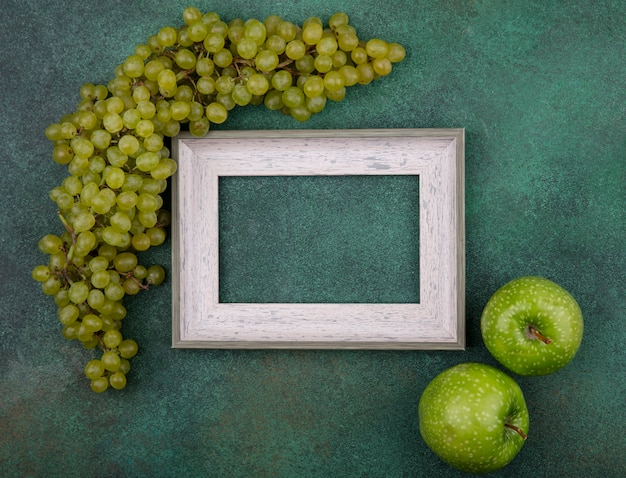 Foto gratuita vista superior del espacio de copia marco gris con uvas verdes y manzanas verdes sobre un fondo verde