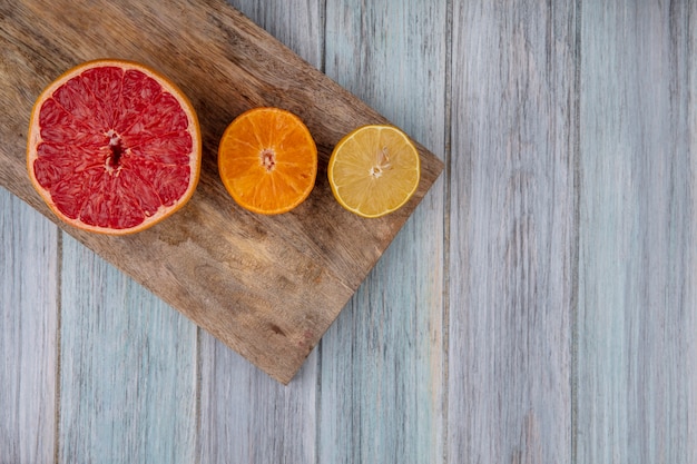 Vista superior del espacio de copia mitad pomelo con mitad naranja y limón en la tabla de cortar contra el fondo gris