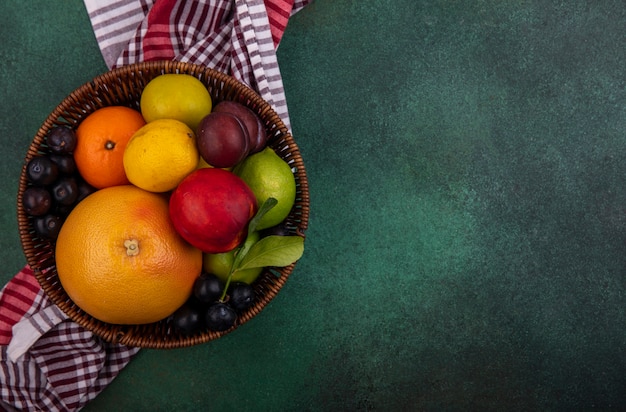 Vista superior espacio de copia pomelo con limón, melocotón, cereza, ciruela, naranja y ciruela en una canasta sobre un fondo verde