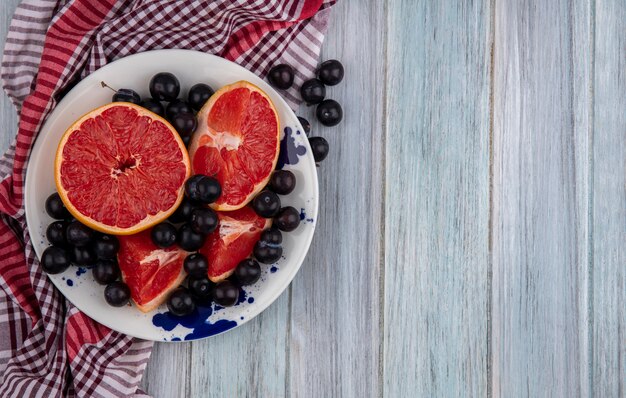 Vista superior espacio de copia pomelo reducido a la mitad con ciruela cereza en un plato sobre una toalla a cuadros sobre un fondo gris