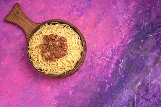 Vista superior de espaguetis cocidos con carne molida en el condimento de pasta de plato de masa de mesa rosa