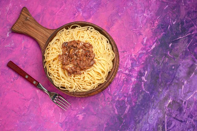 Vista superior de espaguetis cocidos con carne molida en el condimento de plato de masa de pasta de mesa rosa