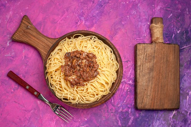 Vista superior de espaguetis cocidos con carne molida en el condimento de plato de masa de pasta de mesa rosa