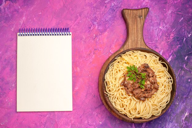 Vista superior de espaguetis cocidos con carne molida en la masa de plato de condimento de pasta de mesa rosa