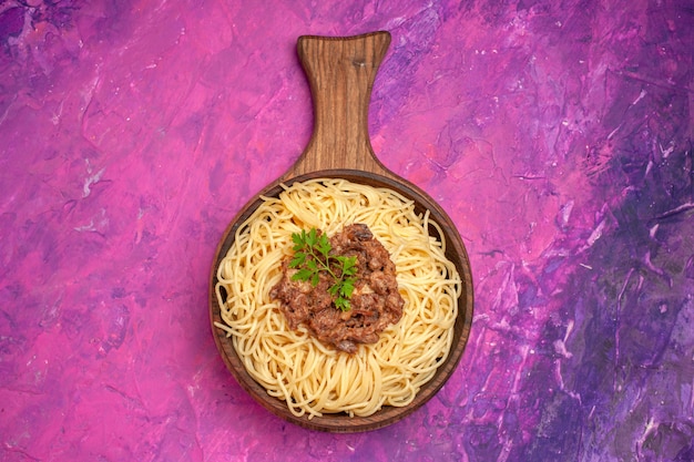 Vista superior de espaguetis cocidos con carne molida en un plato de masa de condimento de pasta de piso rosa