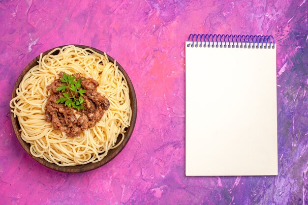 Vista superior de espaguetis cocidos con carne molida en un plato de pasta de pasta de masa de escritorio rosa