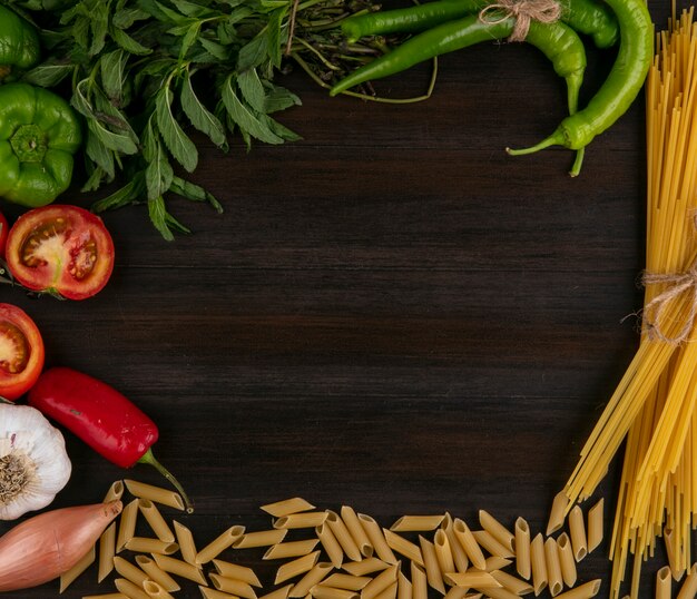 Vista superior de espaguetis crudos con pasta, tomates, pimiento y ajo con menta sobre una superficie de madera