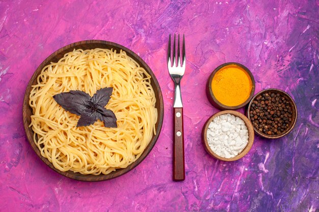 Vista superior de espaguetis deliciosos cocidos con condimentos en pasta de comida de masa de mesa rosa