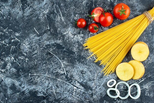 Vista superior de espaguetis con patatas, aros de cebolla y tomates