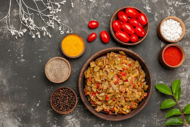 Vista superior de las especias en la mesa cuencos de especias coloridas pimienta negra y tomates junto al plato de judías verdes en la mesa negra